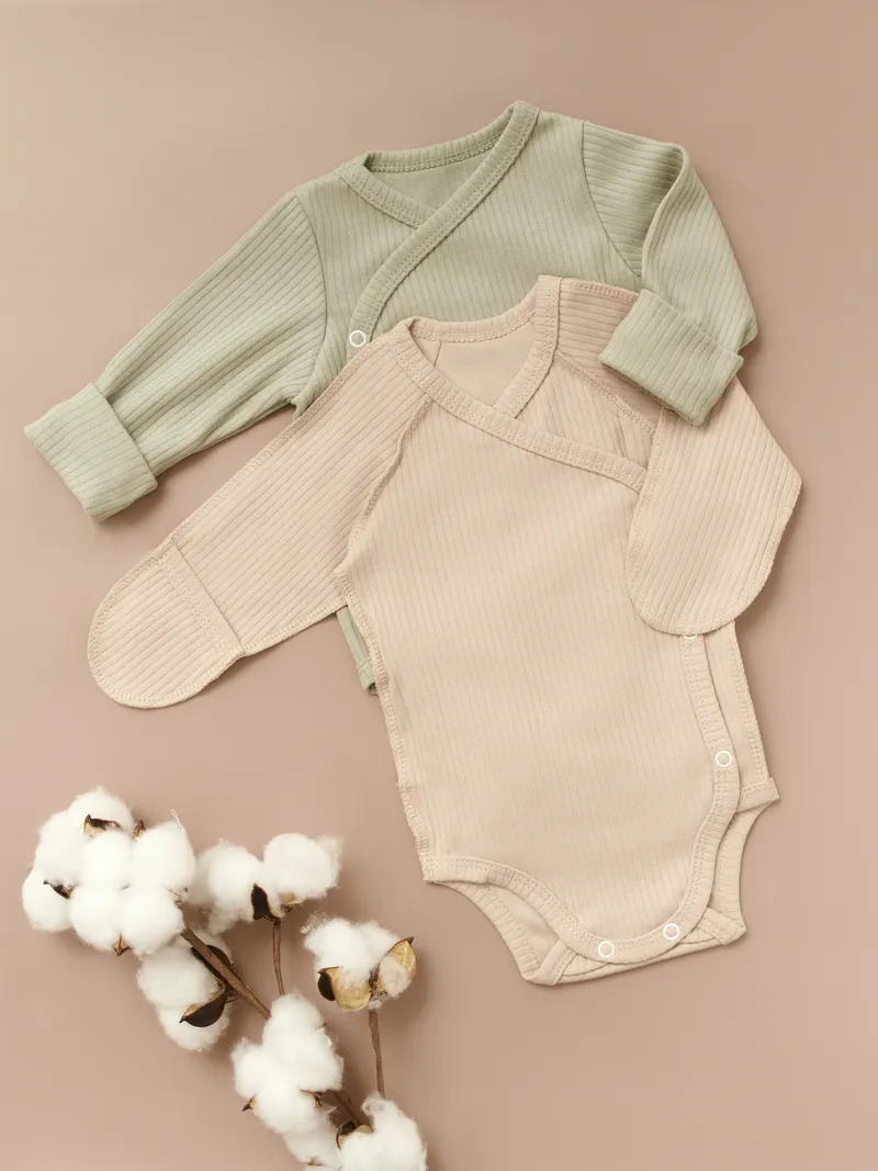 Sage green and beige ribbed baby bodysuits with cotton branch on blush background