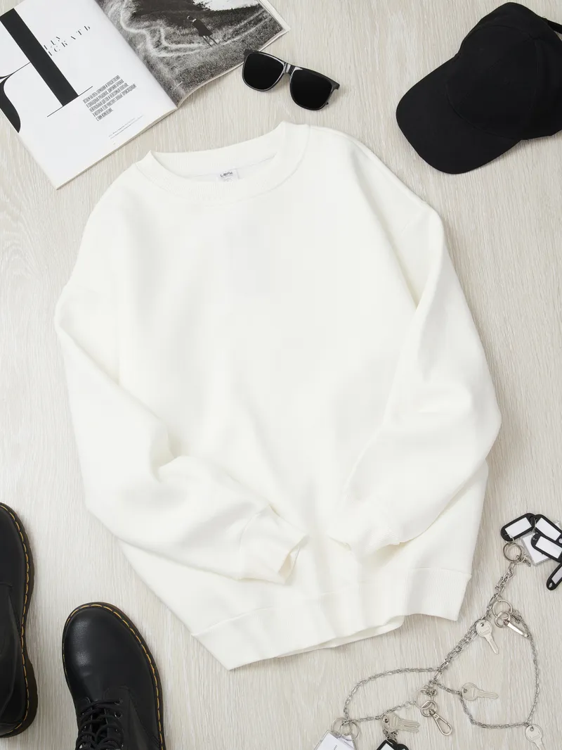 Minimalist monochrome flatlay - white crewneck sweatshirt styled with black sunglasses, cap, boots, keychain, fashion magazine